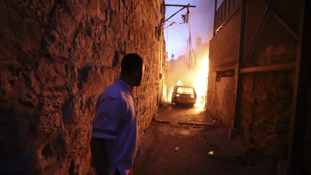 A Palestinian Red Crescent volunteer stands back as fire breaks out in in a house and vehicles during clashes between Israeli troops and Palestinian gunmen in the Old City of Nablus in the northern occupied West Bank early on 24 July 2022. (AFP)
