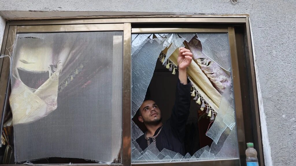 A Palestinian man removes glass shards from a broken window at his home which was damaged by Israeli air strikes in Rafah in the southern Gaza Strip, on 8 August 2022 (AFP)