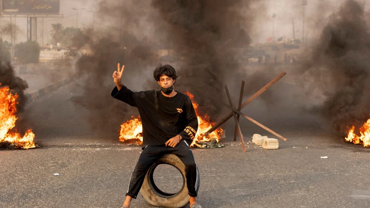 A supporter of Iraqi Shiite cleric Moqtada Sadr poses for a picture on a road blocked with burning tyres during a demonstration in Iraq's southern city of Basra on August 29, 2022 (AFP)