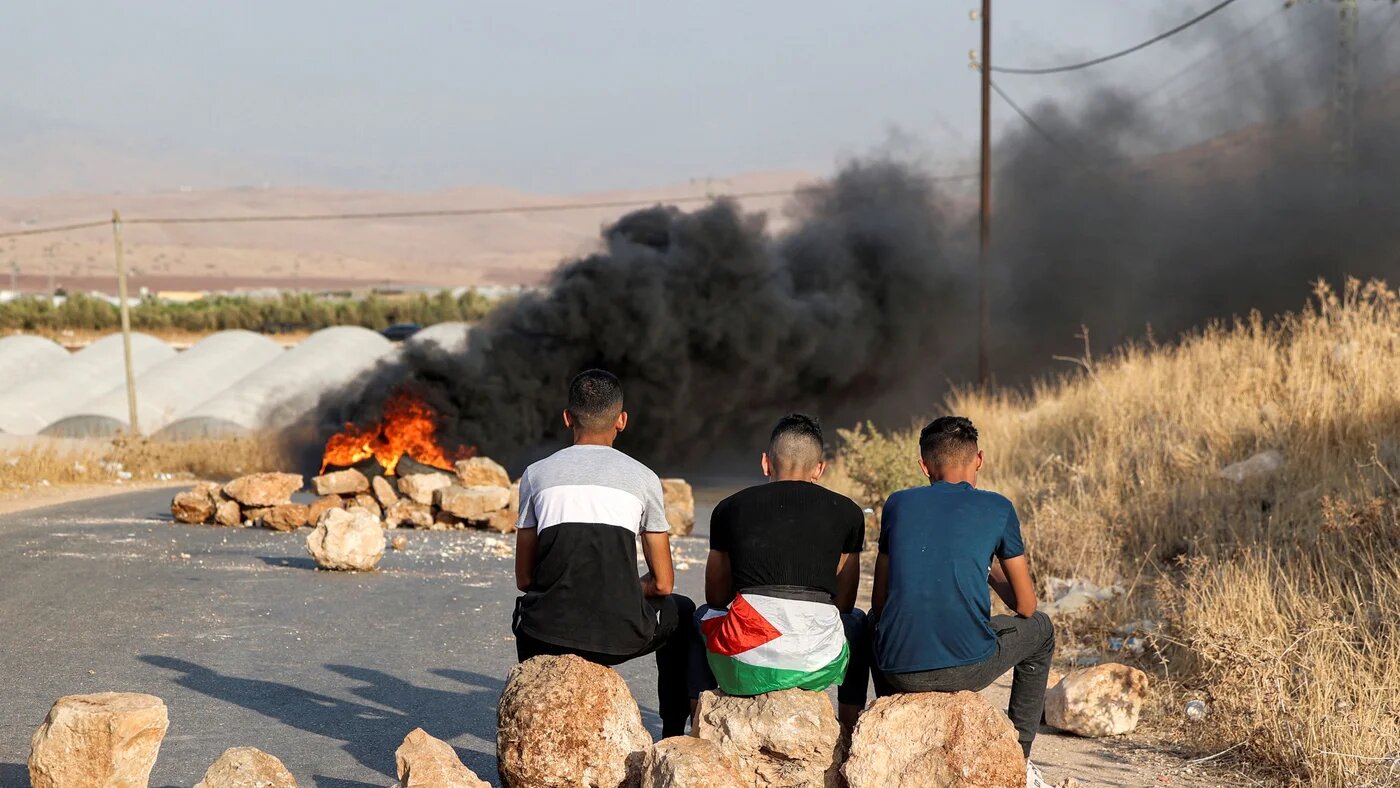 Palestinian men sit on rocks forming a make-shift barricade near flaming tires as they protest against the closure of a road near the site of an attack on an Israeli bus east of the Palestinian city of Tubas in the north of the occupied West Bank on September 4, 2022 (AFP)