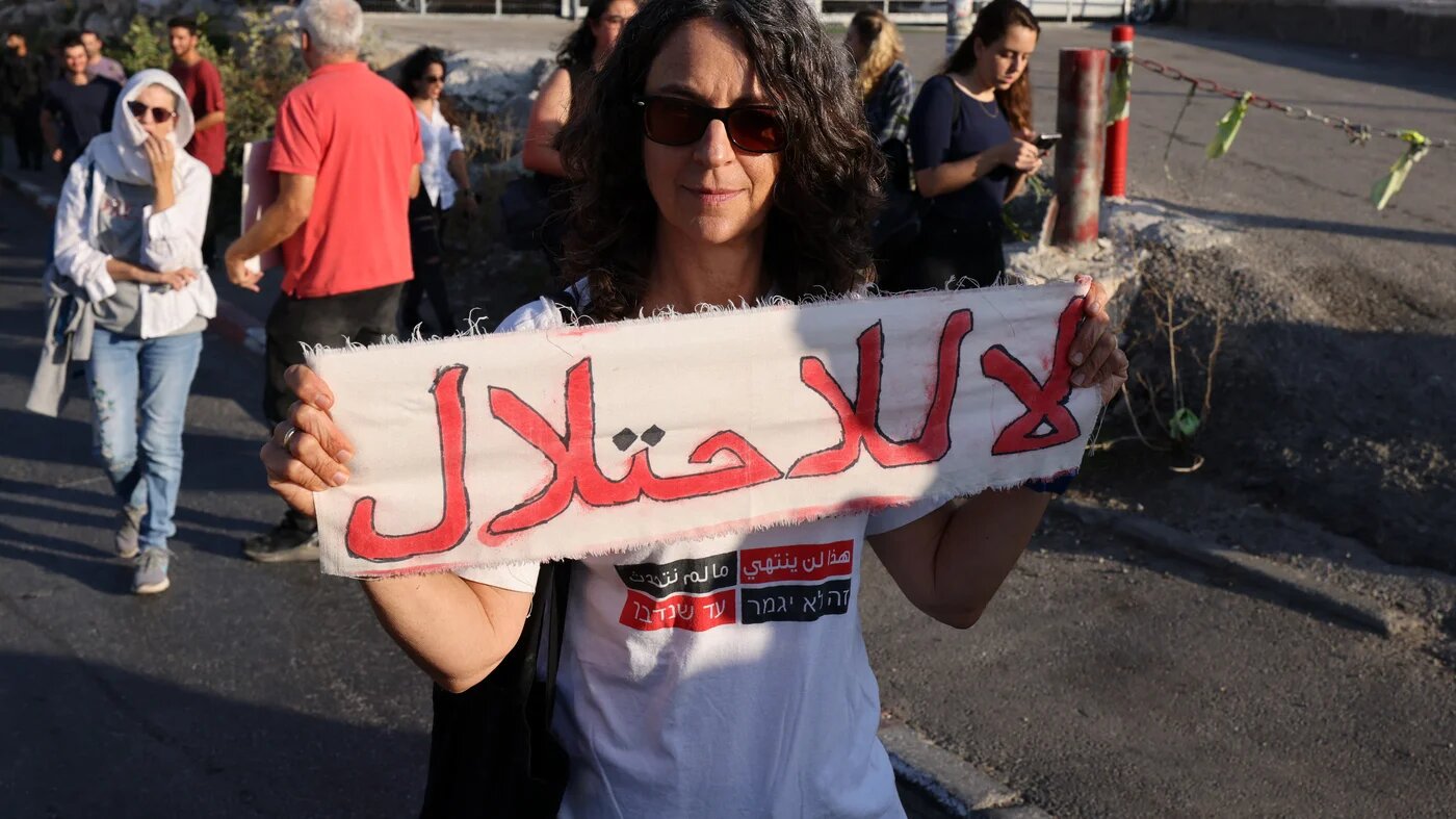 Une femme tient une banderole où est écrit « Non à l’occupation » lors d’un rassemblement organisé par des militants étrangers, palestiniens et israéliens dans le quartier de Sheikh Jarrah à Jérusalem-Est occupée, le 14 octobre 2022 (AFP)