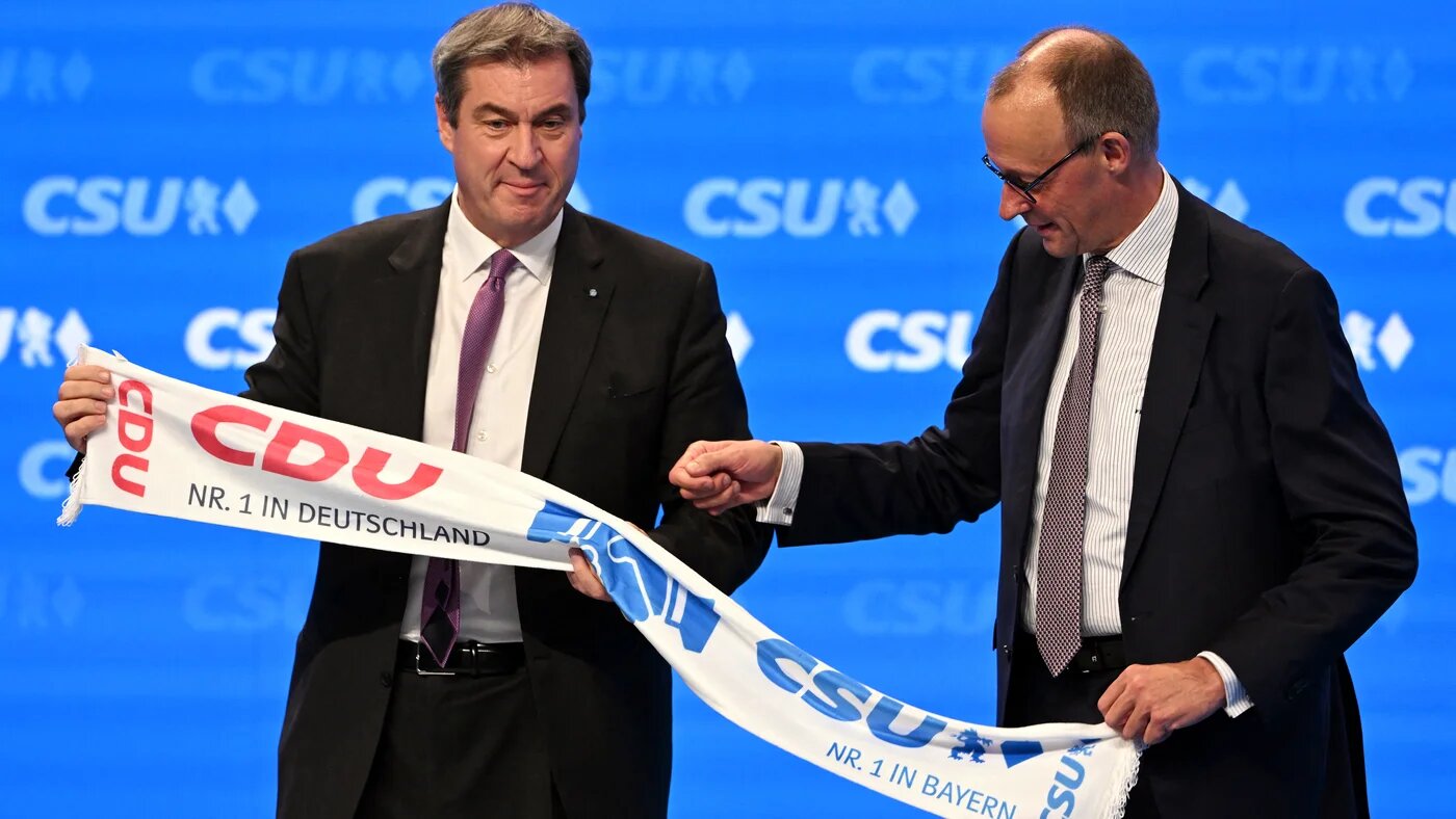 Bavaria's State Premier and leader of the conservative Christian Social Union (CSU) party Markus Soeder (L) and Germany's Christian Democratic Union (CDU) leader Friedrich Merz hold a scarf with their sister parties' logos at the CSU congress in Augsburg, Germany, on 29 October 2022 (AFP)