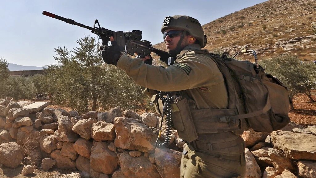 An Israeli soldier takes aim at Palestinians during a protest against the establishment of Israeli outposts, in Beit Dajan, east of the occupied West Bank city of Nablus, on 4 November 2022 (AFP)