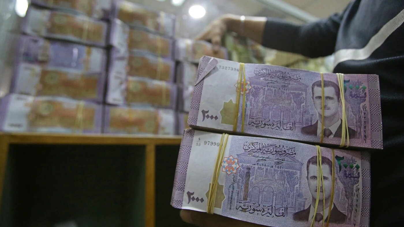An employee piles up stacks of Syrian lira banknotes at the Commercial Bank of Syria in Damascus (AFP)