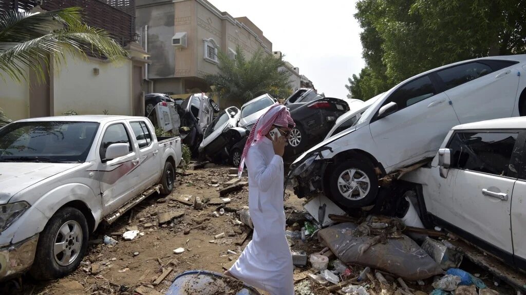A man walks past cars piled up in a street after they were washed away by heavy rains in the Saudi coastal city of Jeddah on 25 November 2022 (AFP)
