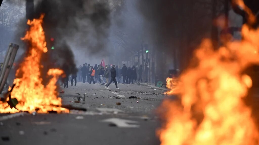 Protesters stand behind flames during clashes following a demonstration a day after a gunman opened fire at a Kurdish cultural centre killing three people, at The Place de la Republique in Paris on 24 December 2022 (AFP)