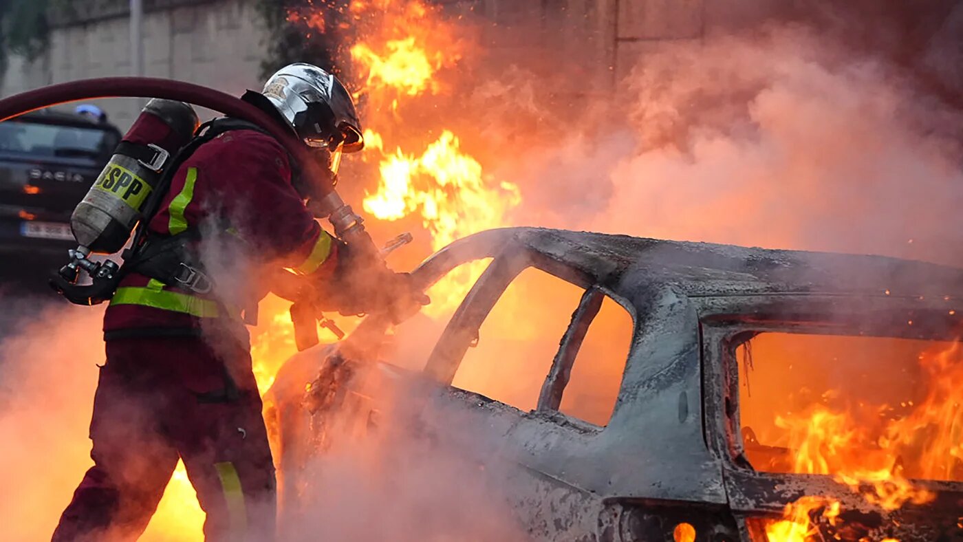 Firefighter extinguish a burning vehicle destroyed during protests in Nanterre, west of Paris, on 27 June (AFP)