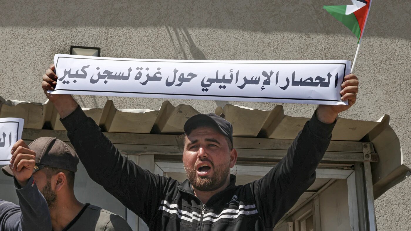A Palestinian man holds a banner reading 'The Israeli siege has turned Gaza into a big prison' at a protest against the blockade near the Kerem Shalom crossing in Rafah, southern Gaza, on 10 August 2023 (Said Khatib/AFP)