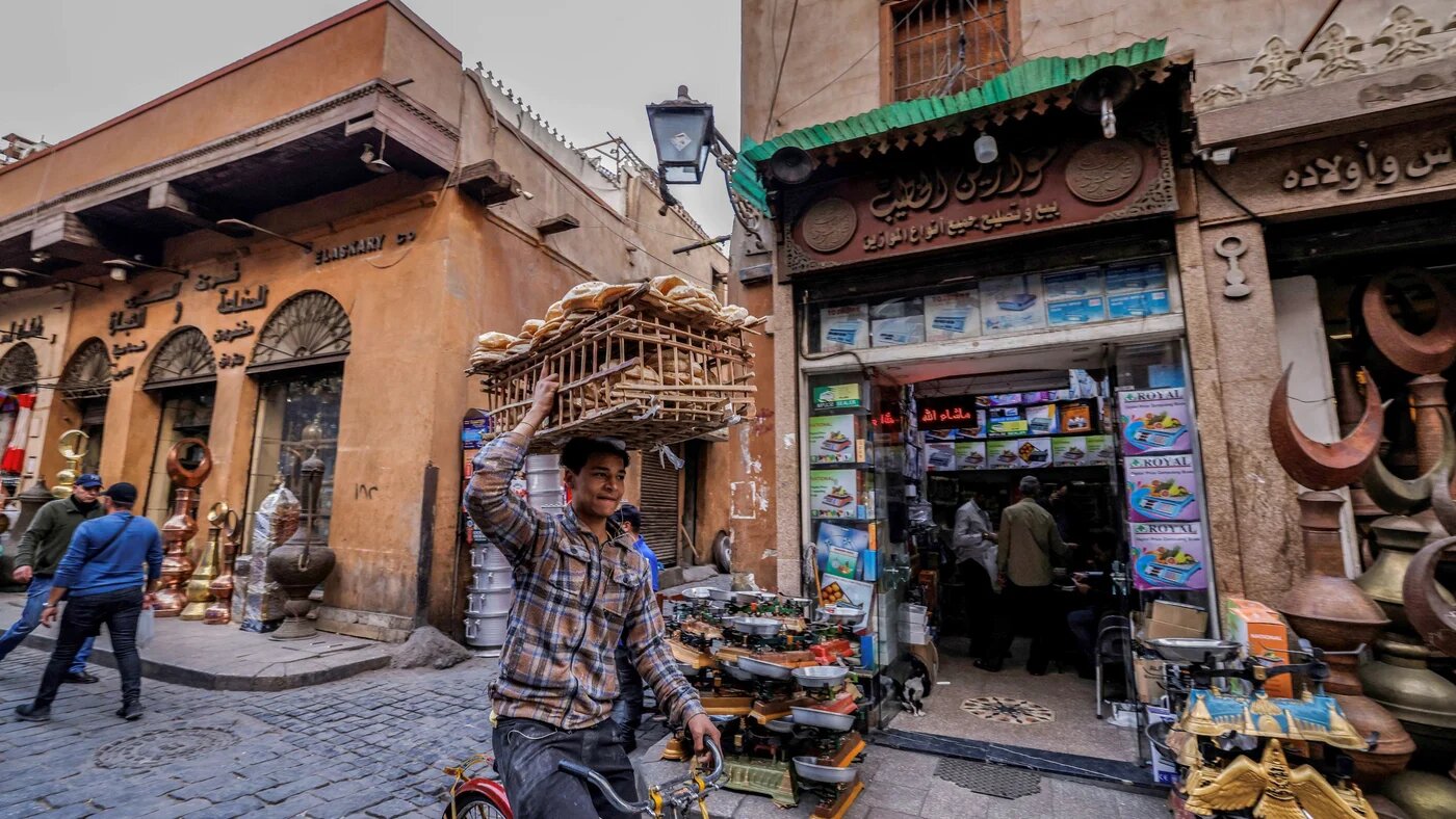 A deliveryman balances a load of bread on his head as he cycles through the old quarters of Cairo