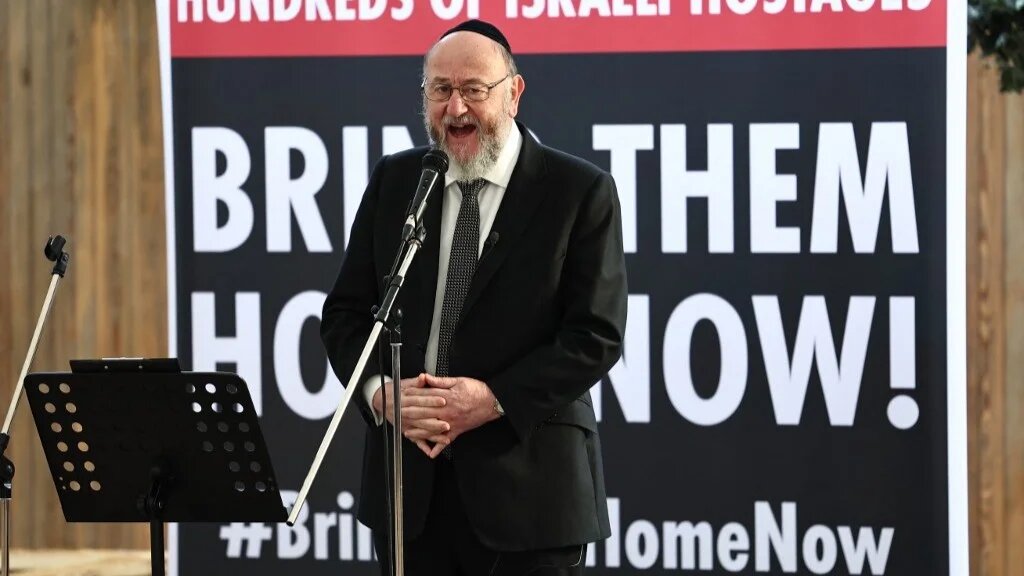 Chief Rabbi Ephraim Mirvis speaks to people viewing the empty places laid out for the 220 hostages at a 'Shabbat' table in the JW3 Piazza in north London on October 27, 2023 (AFP)