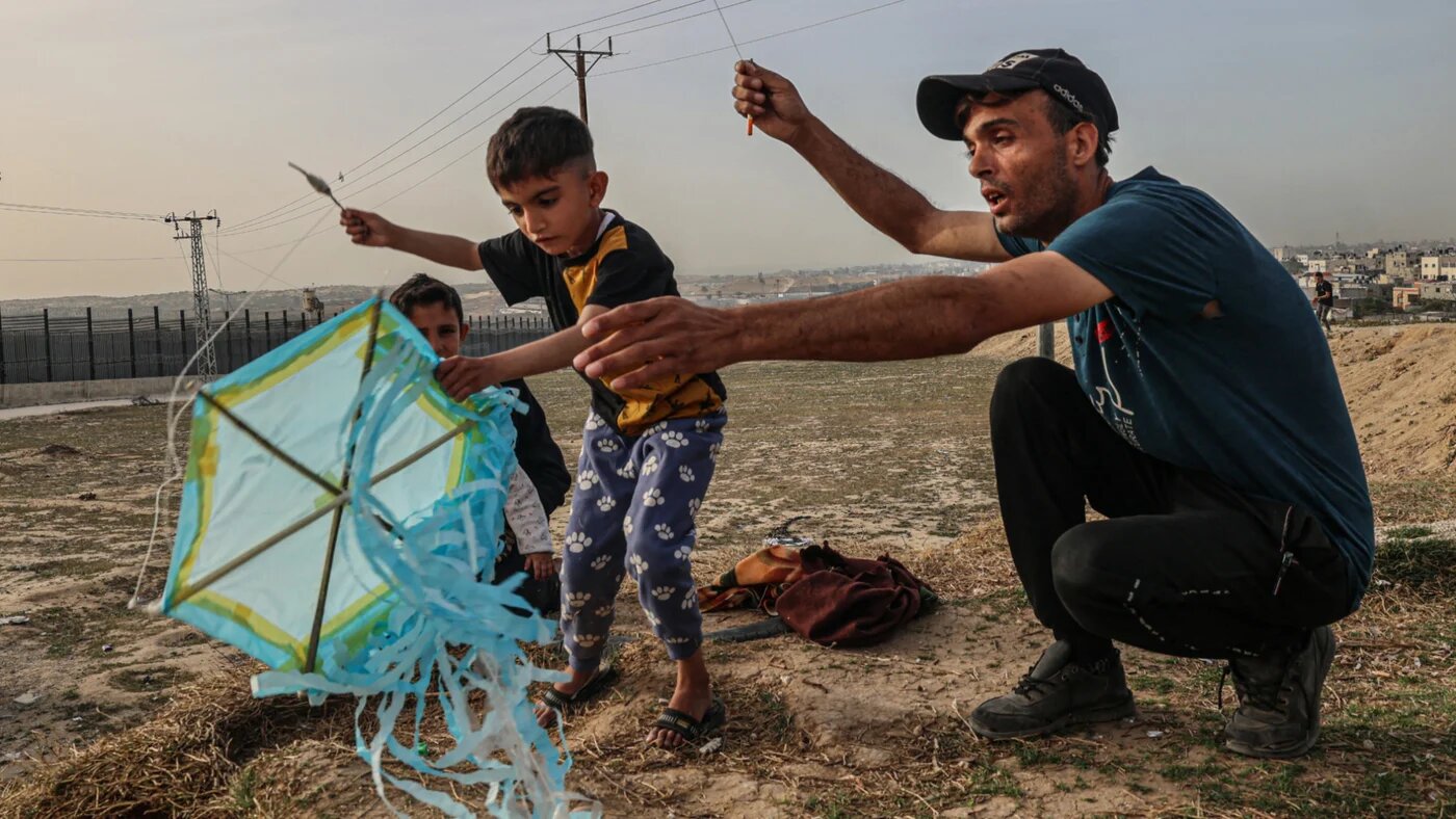 A displaced Palestinian man helps a child to fly a kite near the border with Egypt in Rafah in the southern Gaza Strip on 28 March 2024 (Said Khatib/AFP)