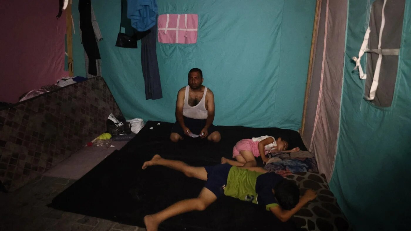 A displaced Palestinian family rests in a tent at night during a heatwave at al-Bureij refugee camp in the central Gaza Strip on 26 June 2024 (Eyad Baba/AFP)