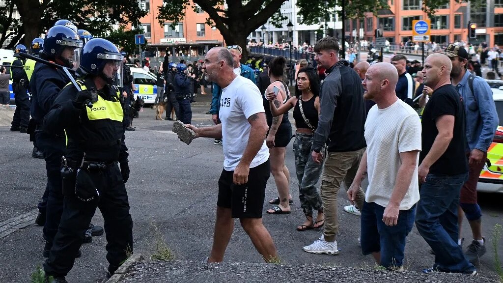 A protester holding a piece of concrete walks towards riot police as clashes erupt in Bristol on August 3 2024 (AFP)