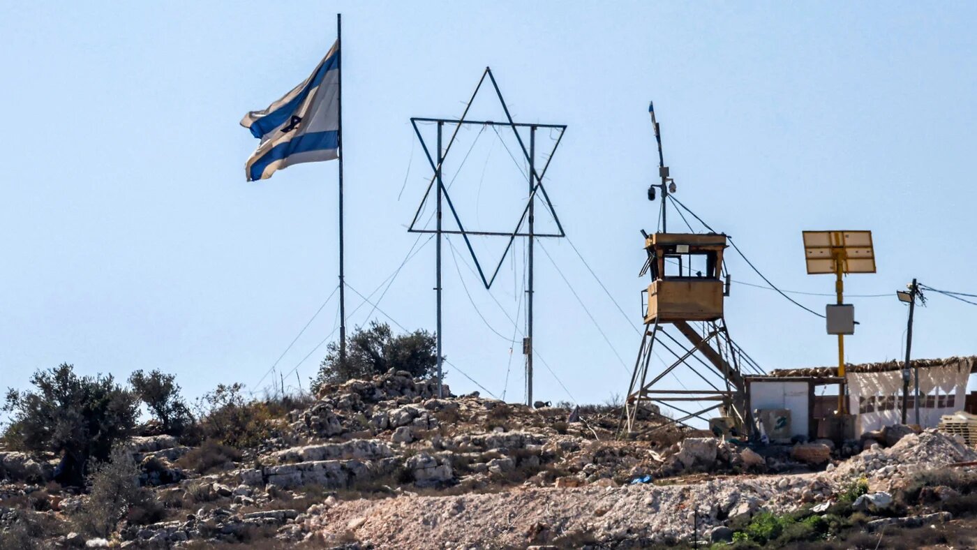An Israeli flag and a giant Star of David are displayed next to an Israeli watchtower in the Eviatar settlement outpost opposite the village of Beita, south of Nablus in the occupied West Bank, on 19 October 2024 (AFP/Jaafar Ashtiyeh)