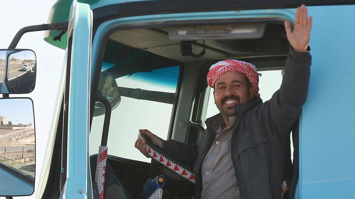 A Jordanian man waves as he waits to cross into Syria through the Jaber-Nassib border crossing after the Jordanian government allowed for the transport of goods to resume, on 19 December 2024 (AFP/Khalil Mazraawi)