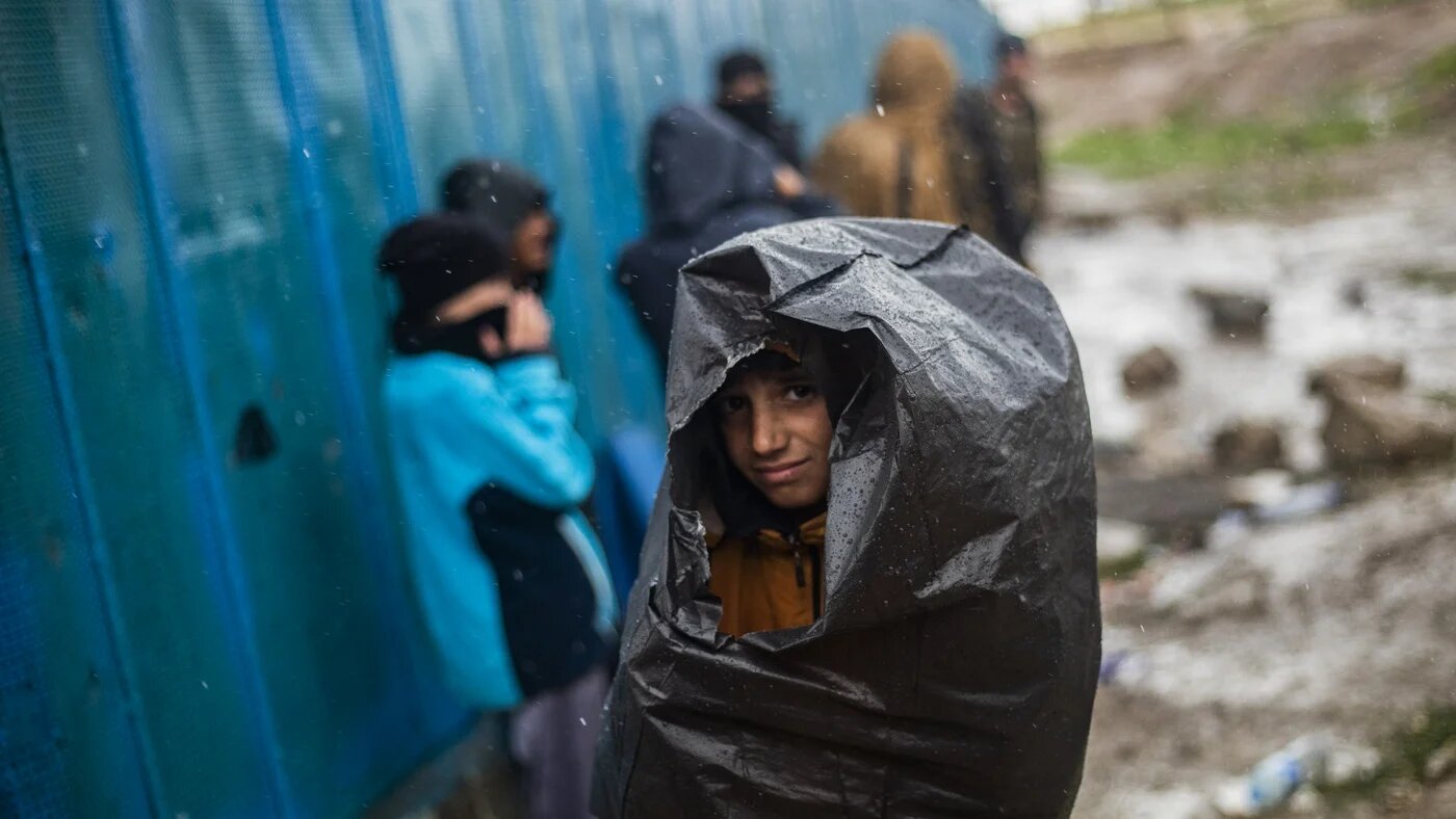 A boy shelters from the rain with a plastic bag during a military operation at Camp Roj in Syria's Hasakah province, 5 April 2025 (Delil Souleiman/AFP)