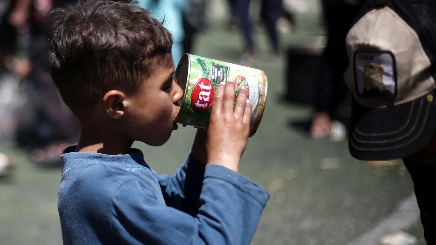 A Palestinian child eats his portion of a hot meal at a free food distribution point at the Nuseirat refugee camp, central Gaza Strip, on 19 April 2025 (AFP/Eyad Baba)