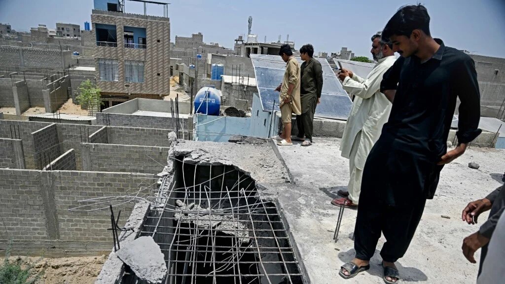 Residents gather over the roof of a damaged house at the site where an alleged drone was shot down in Karachi on 8 May (AFP)