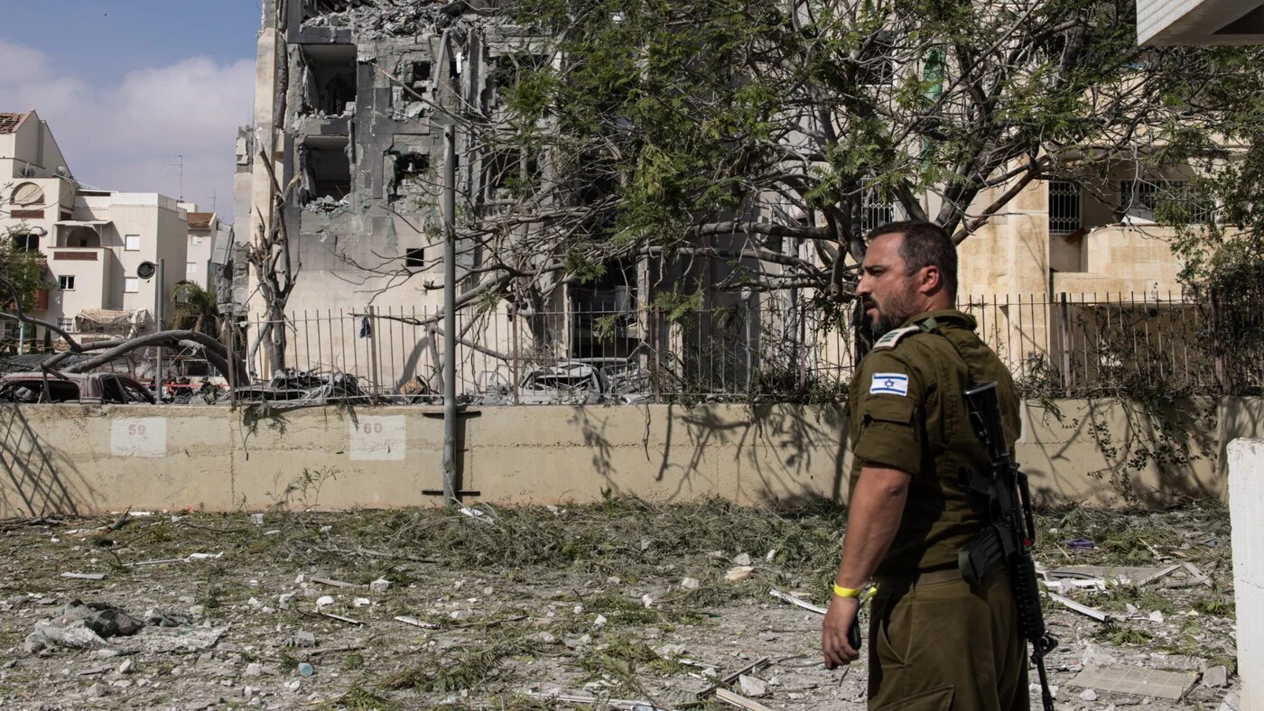 Israeli soldier stands guard as rescuers search for casualties in the rubble of a building hit by an Iranian missile in Beersheba in southern Israel on 24 June (AFP/John Wessels)