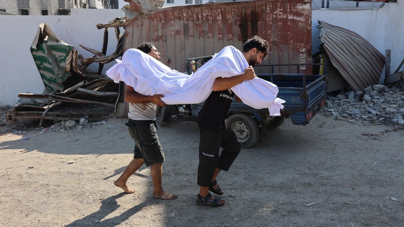 Palestinian men carry the body of a person killed while waiting for aid outside al-Shifa Hospital in Gaza City on 3 July 2025 (Omar al-Qattaa/AFP)