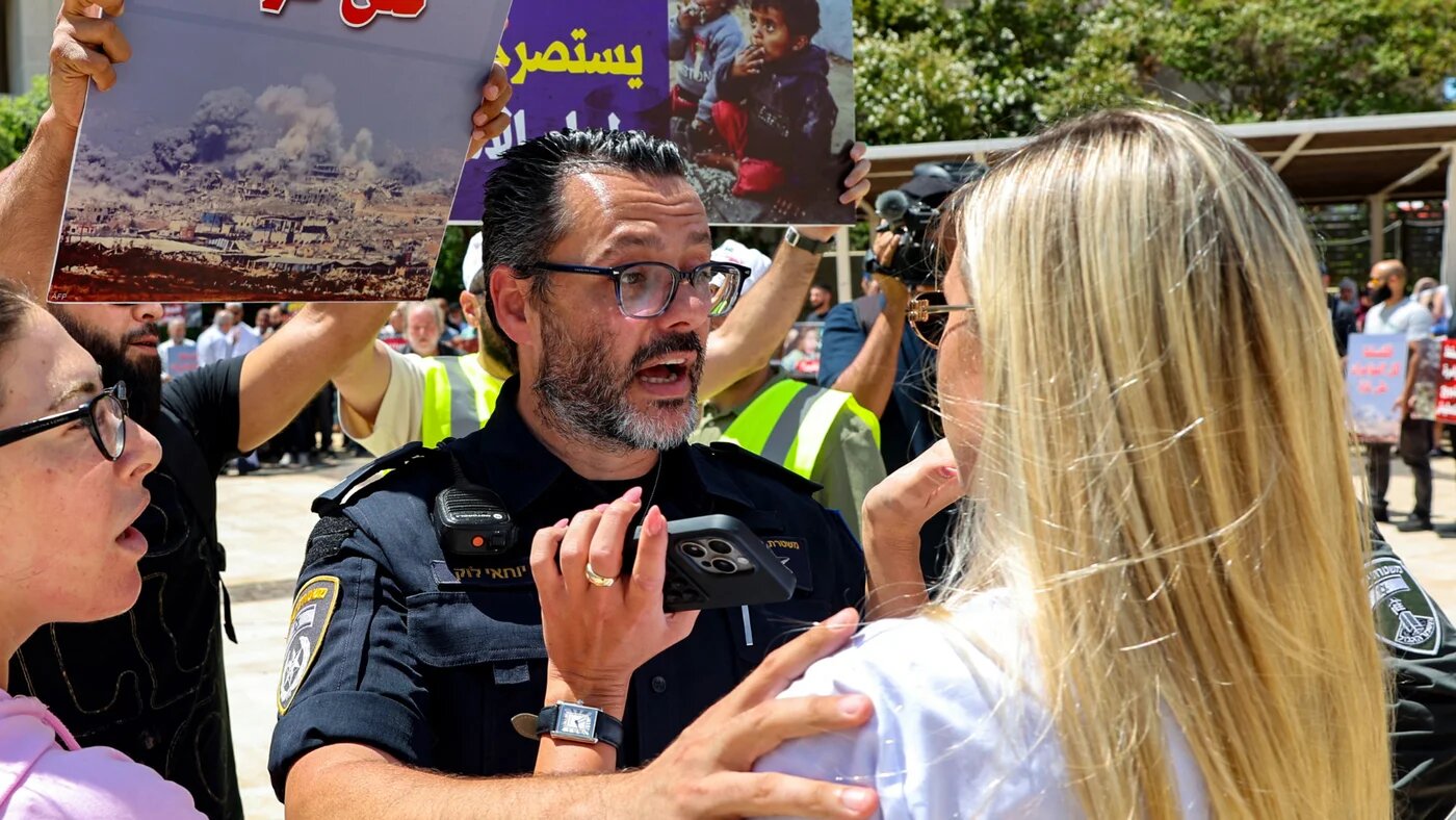 An Israeli police officer confronts a woman trying to stop a protest against the closure of the Rafah crossing and the catastrophic humanitarian situation in the Gaza Strip on 31 July 2025 (AFP/Jack Guez)
