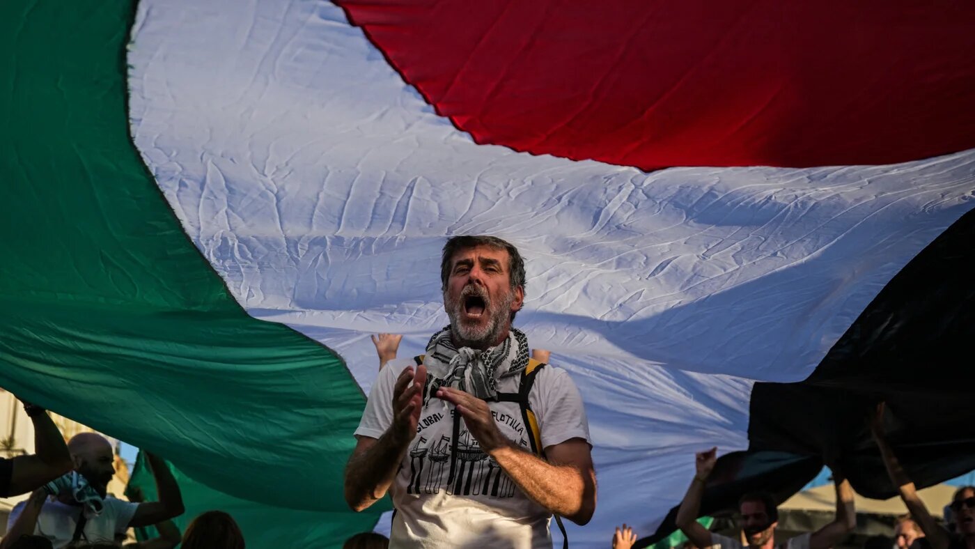 A man protests beneath a Palestinian flag on Spyros Island before two vessels depart for the Global Sumud Flotilla to deliver aid to Gaza, 14 September 2025 (AFP/Aris Messinis)