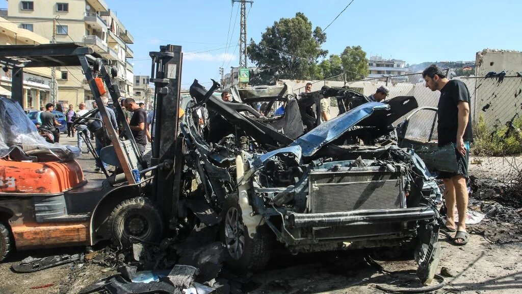 People gather around a destroyed car targeted in an Israeli drone attack in the southern Lebanese village of Zebdine, on October 6, 2025. (AFP)