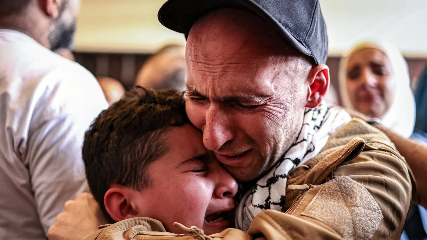 A released Palestinian prisoners embraces a boy upon arrival by bus at Ramallah Cultural Centre in Ramallah in the occupied West Bank, on 13 October 2025 (AFP/Zain Jaafar)