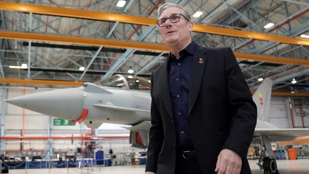 Britain's Prime Minister Keir Starmer passes a Eurofighter Typhoon fighter jet during a visit to BAE Systems in Warton, near Preston, northern England, on October 28, 2025.