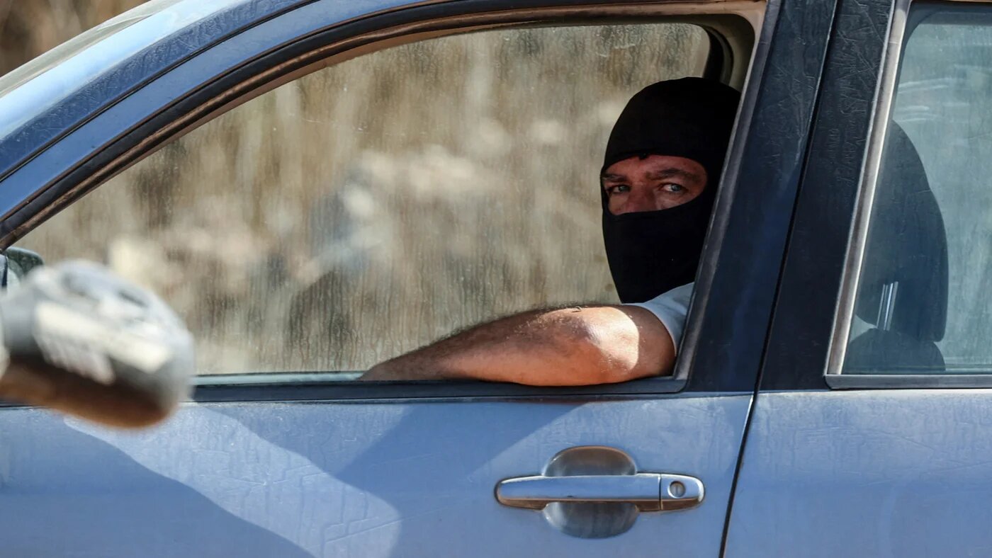 An Israeli settler sits in his car as he watches others disrupt Palestinian farmers' olive harvest near the Israeli occupied Palestinian West Bank village of Turmus Ayya, near  Ramallah on 28 October 2025 (AFP/Zain Jaafar)