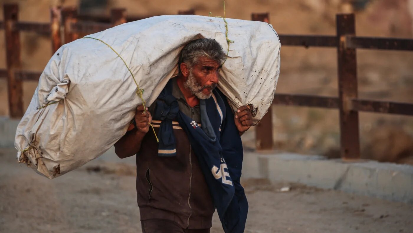 A Palestinian man carries his belongings along a bridge in Nuseirat, Gaza Strip on 11 November 2025 (AFP/Eyad Baba)