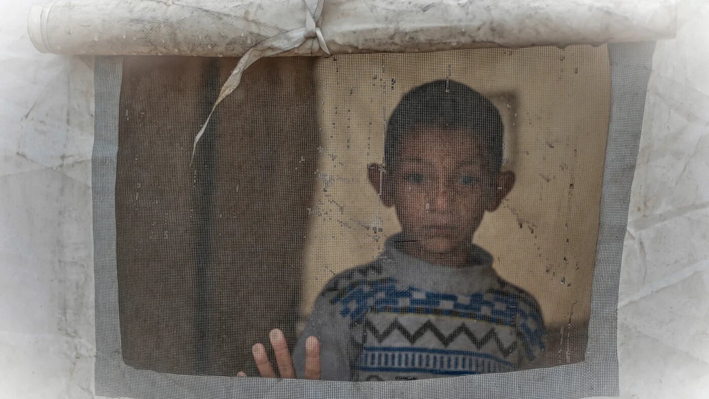 A boy looks out from a tent at a makeshift camp sheltering displaced Palestinians after heavy rains in Gaza City on 11 December 2025 (AFP/Omar al-Qattaa)