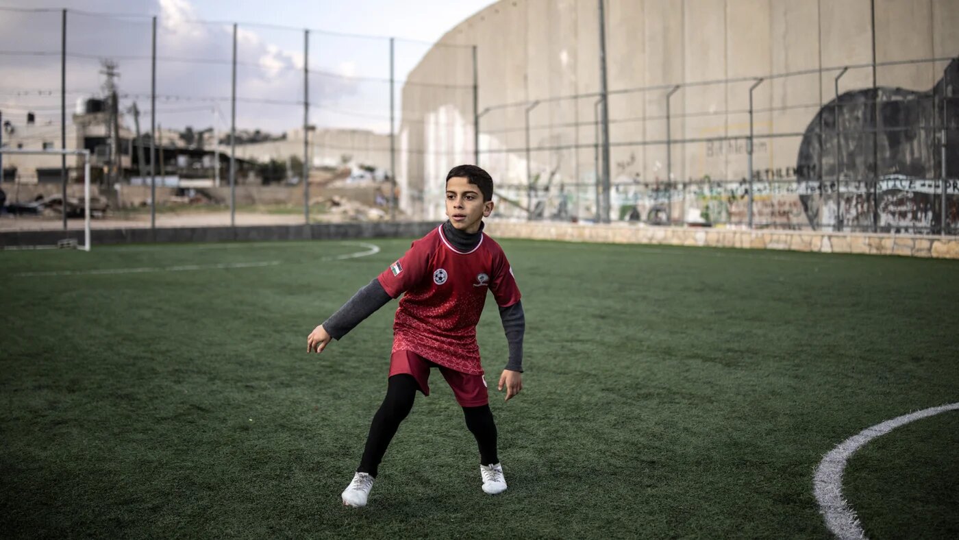 A displaced Palestinian youth takes part in a training session at the Aida Refugee Camp’s football pitch, next to the separation wall outside Bethlehem in the occupied West Bank, on 16 December 2025 (AFP/John Wessels)