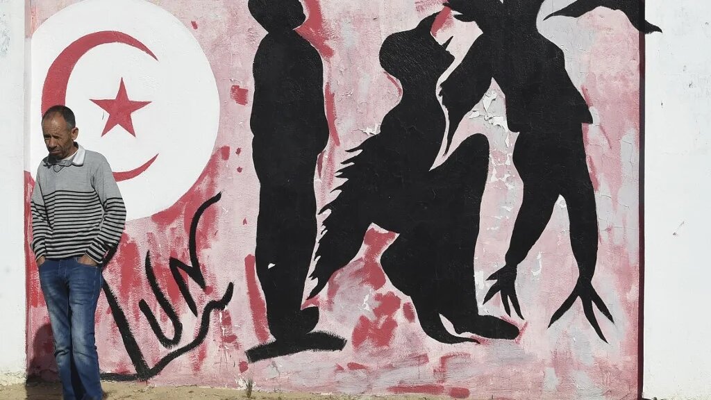 Un Tunisien attend près d’un graffiti représentant les silhouettes d’un homme se métamorphosant en oiseau symbolisant la liberté, place Mohamed Bouazizi, au centre de la ville de Sidi Bouzid le 27 octobre 2020, berceau de la révolution tunisienne de 2011 (AFP)