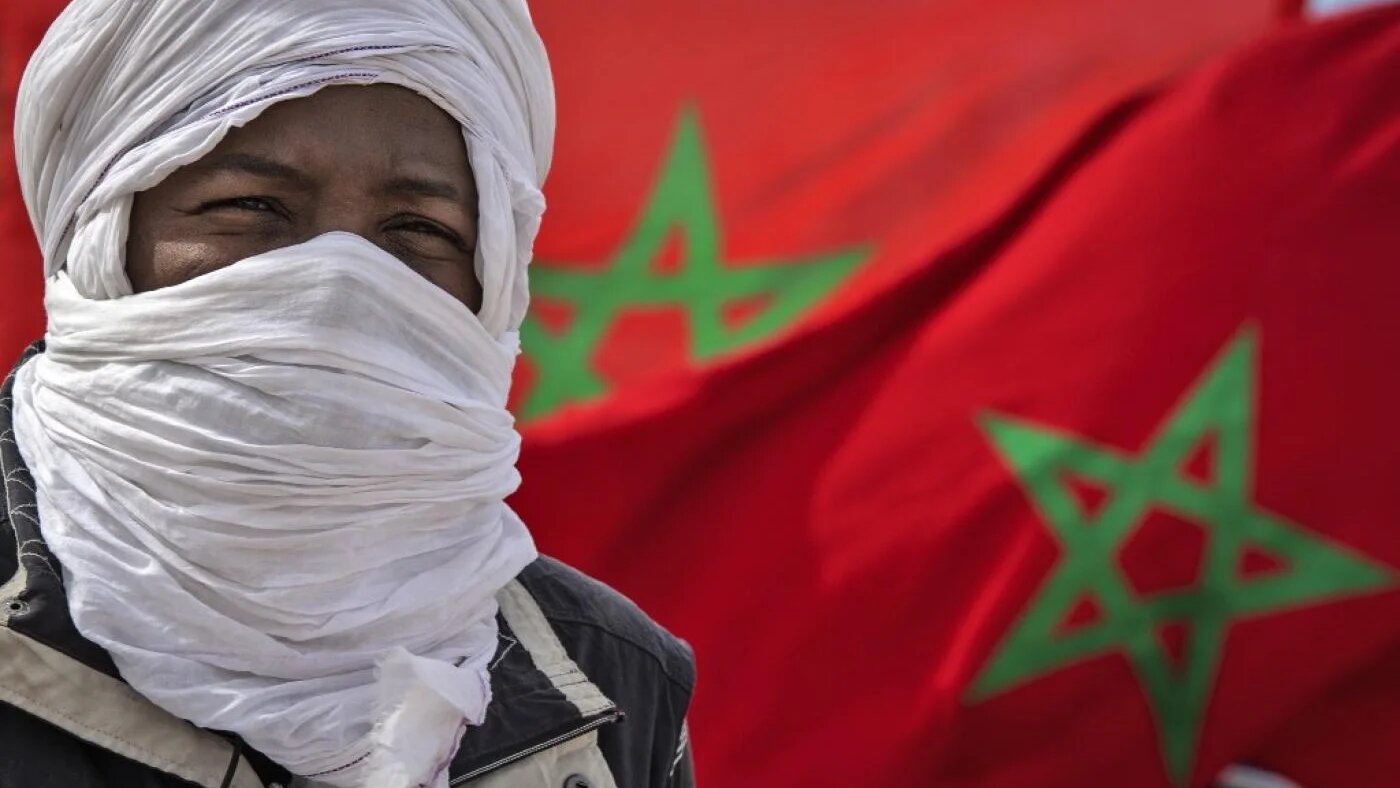 Un membre d’une tribu se tient devant des drapeaux marocains près de la frontière à Guerguerat, le 26 novembre 2020 au Sahara occidental, après l’intervention des Forces armées royales marocaines dans la région (AFP)