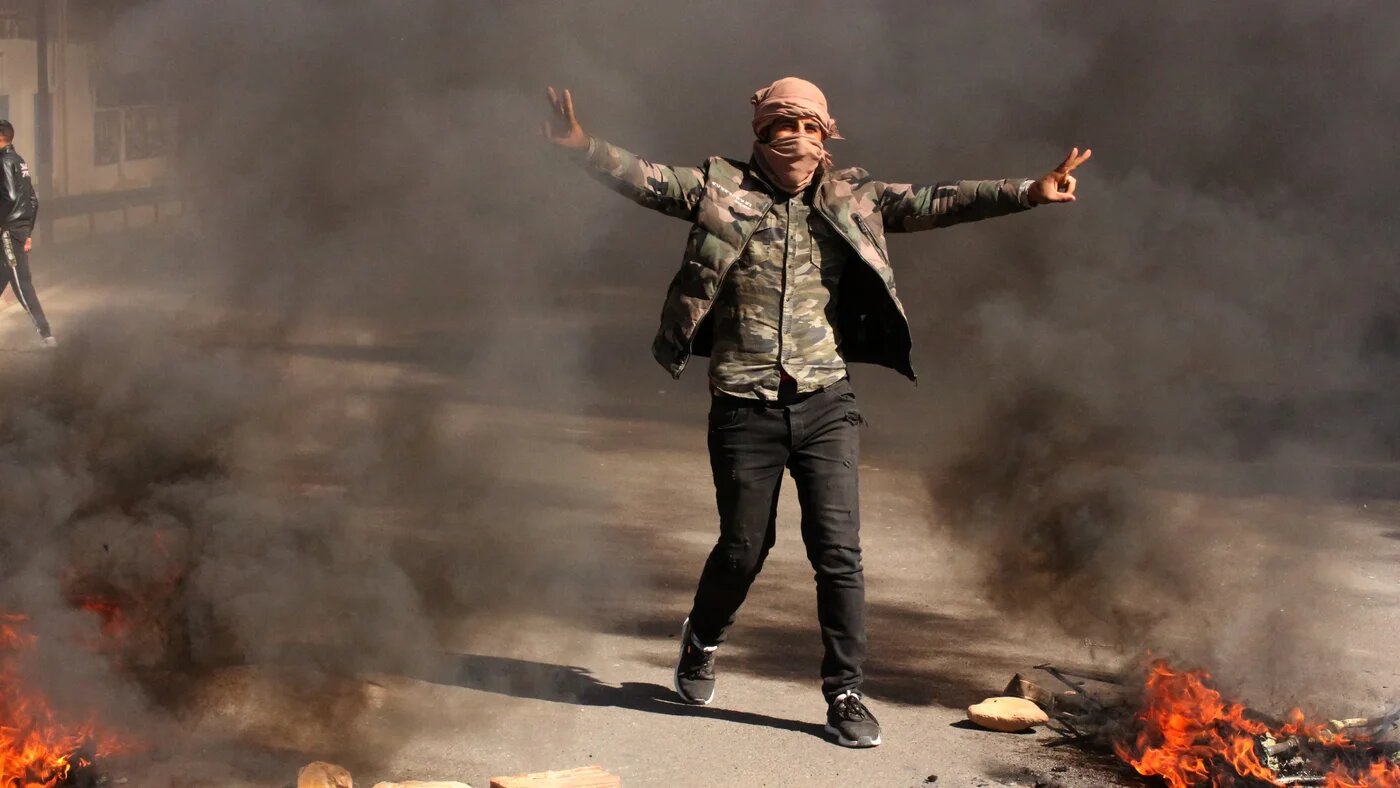 Un Tunisien fait le V comme signe de victoire alors que des jeunes brûlent des pneus et bloquent des routes dans la ville de Tataouine, au sud du pays, le 12 février 2021 (AFP)