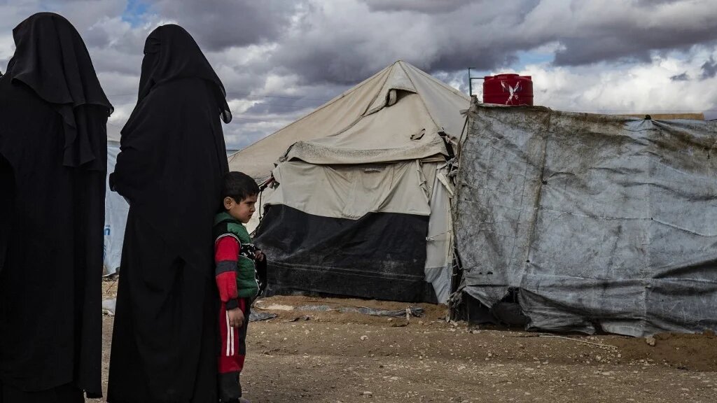 Des femmes et un enfant se tiennent près des tentes du camp kurde d’al-Hol qui abrite des proches présumés de combattants du groupe État islamique (Delil Souleiman/AFP)