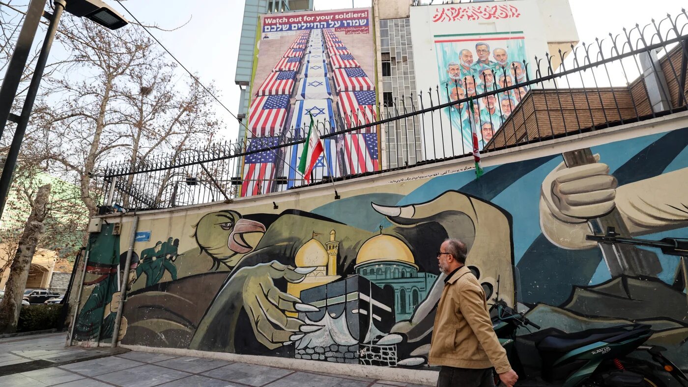 An Iranian man walks past an anti-US and anti-Israel banner hanging on a building in Palestine Square, after the United States announced the deployment of a naval strike group to the region, in Tehran, on 27 January 2026 (Atta Kenare/AFP)