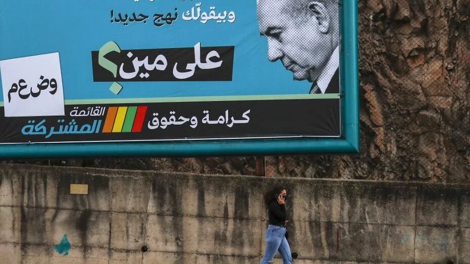 A women walks past an electoral billboard by the Joint List depicting Benjamin Netanyahu with a slogan reading in Arabic "the father of the nation-state law, says "a new approach", whom is he fooling? " in the northern city of Nazareth ahead of the March 2021 election. (AFP)