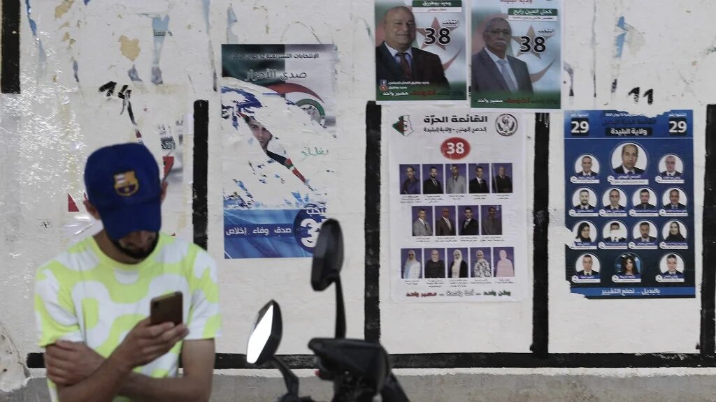 Un Algérien consulte son téléphone devant des panneaux électoraux, le 31 mai 2021 (AFP)