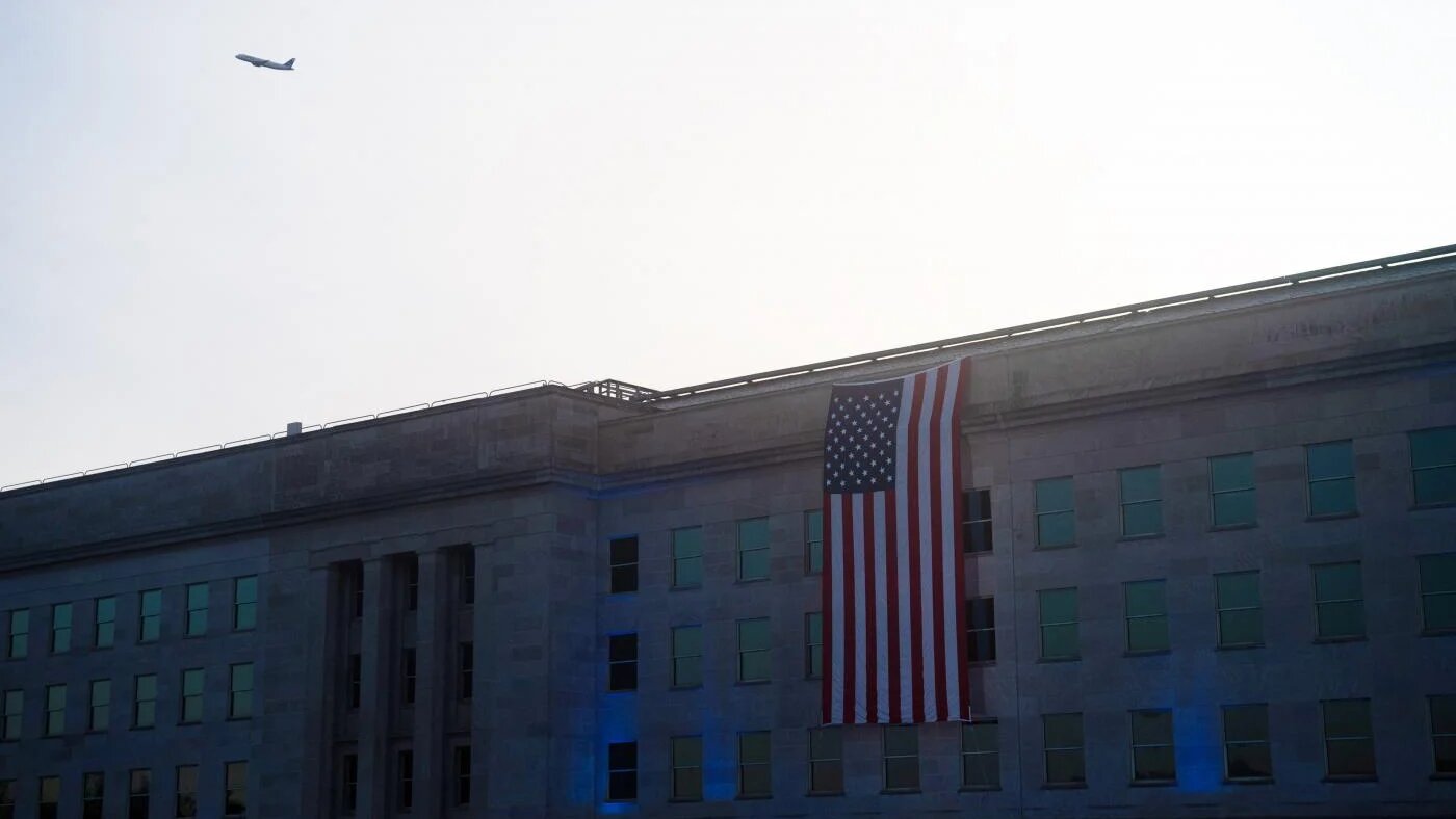 Un drapeau américain recouvre la façade du Pentagone, à Washington D.C., pour commémorer le 20e anniversaire des attentats du 11-Septembre, tandis qu’un avion passe dans le ciel, le 11 septembre 2021 (AFP)