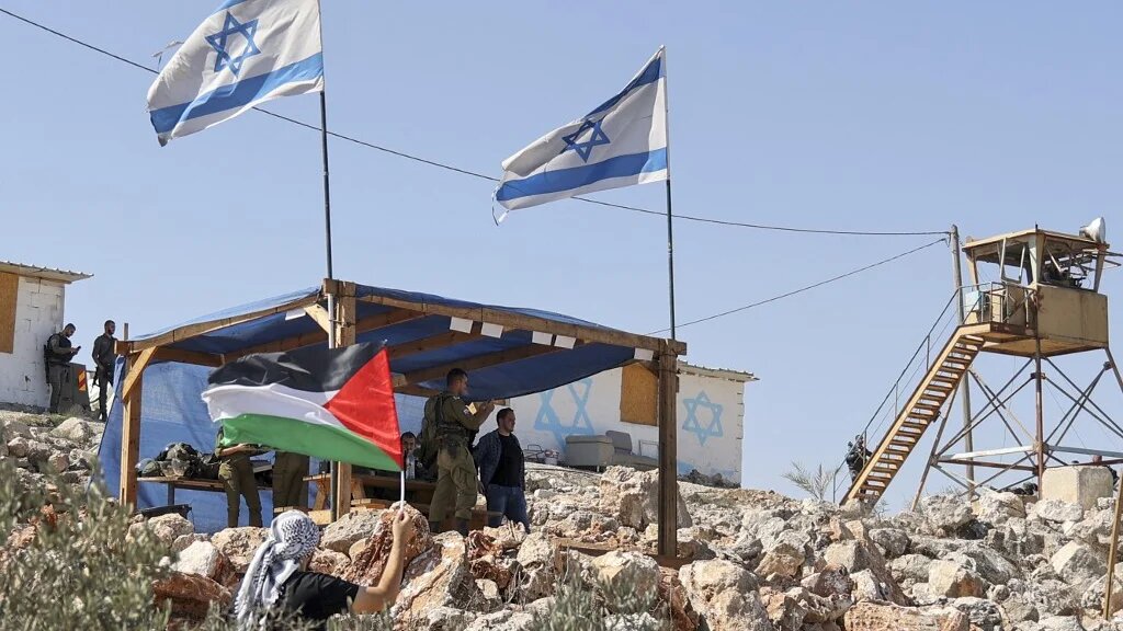 A Palestinian man waves his country's flag next to the Israeli settlement outpost of Evitar in the village of Beita, north of Nablus in the occupied West Bank, on 10 October 2021 (AFP)
