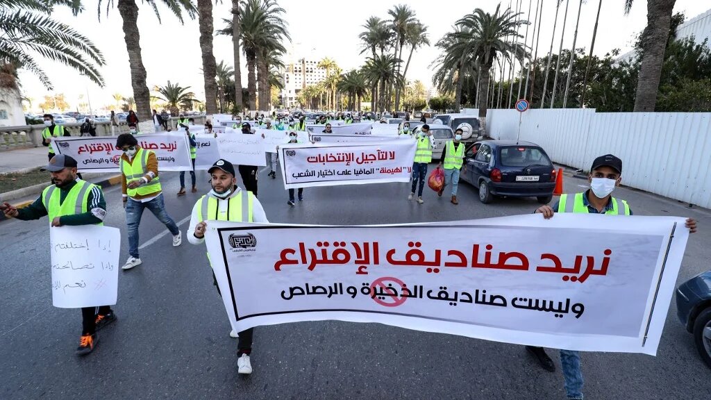 De jeunes militants libyens manifestent contre le report des élections présidentielles sur la place des Martyrs de la capitale Tripoli, le 25 décembre 2021. La banderole dit en arabe : « Nous voulons des urnes, pas des boîtes de munitions ». (AFP/Mahmud Turkia) 