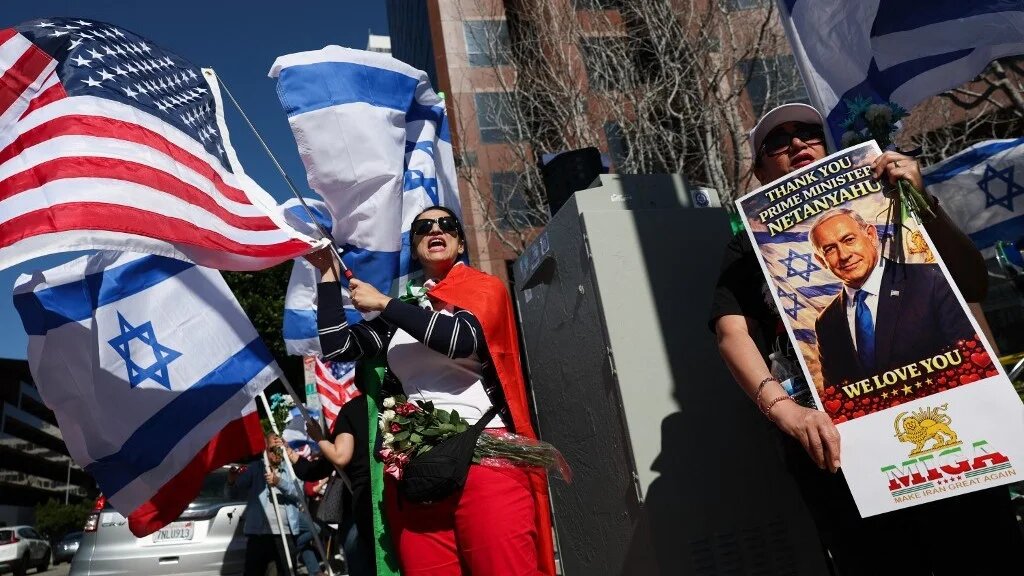 A person holds a sign supporting Israeli Prime Minister Benjamin Netanyahu as people wave flags and chant during a gathering of Iranian monarchists outside the Consulate General of Israel in Los Angeles, on 5 March 2026 (Patrick T Fallon/AFP)