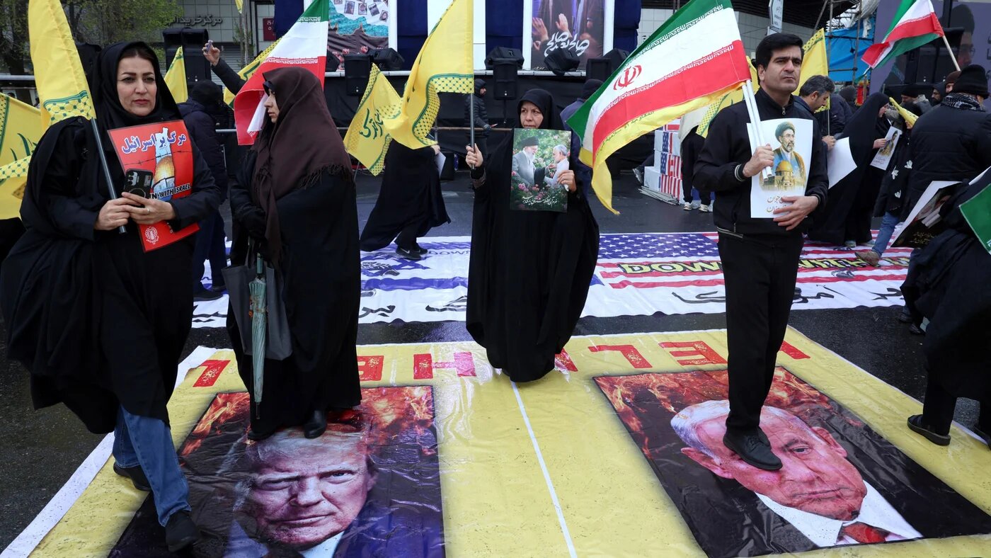 An Iranian woman walks across posters of US President Donald Trump (L) and Israeli Prime Minister Benjamin Netanyahu during an al-Quds (Jerusalem) Day rally in Tehran on 13 March 2026, weeks after US-Israeli strikes on Iran triggered a regional war (AFP)
