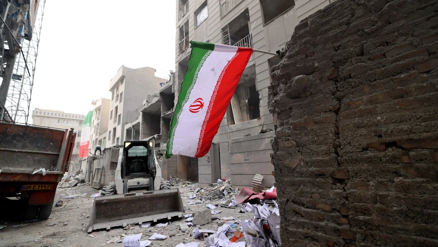 An Iranian flag flutters as a digger arrives to remove debris from buildings destroyed in US-Israeli military strikes on the capital Tehran, on 15 March 2026 (Atta Kenare/AFP)
