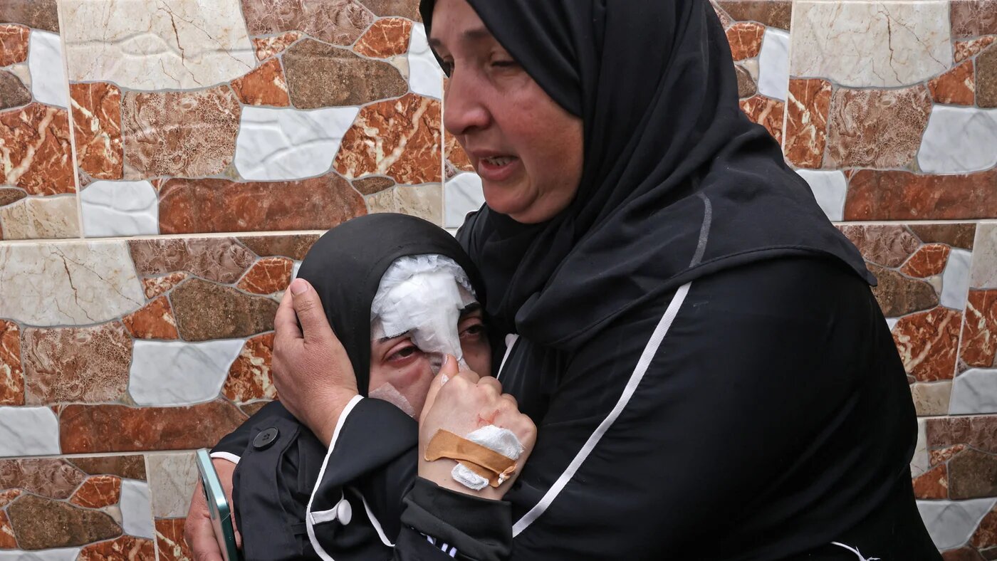 A woman comforts an injured girl as they mourn the death of the four Palestinian women killed from missile shrapnel that hit the Beit Awa town near the occupied West Bank city of Hebron on 19 March 2026 (AFP/Hazem Bader) 