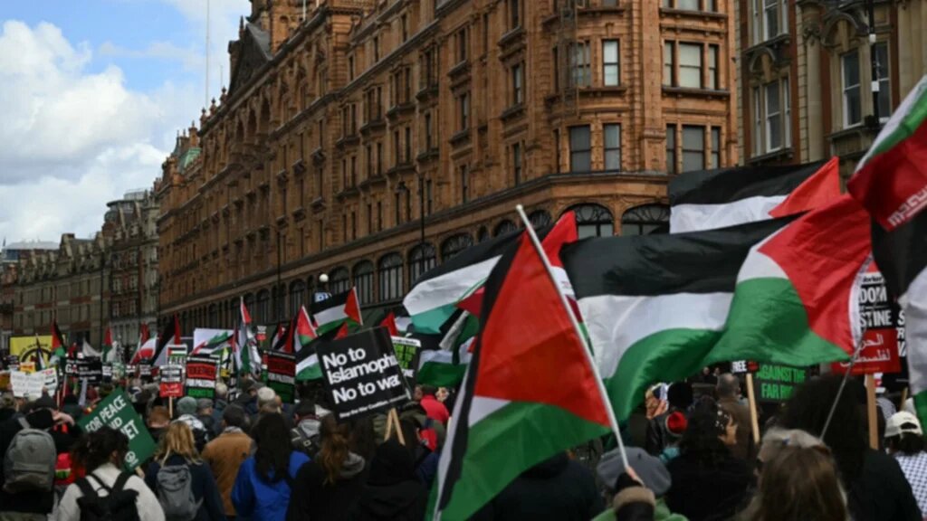 Protesters hold placards and wave Palestinian flags as they march past Harrods department store during a march organised by the Palestine Coalition in central London on March 28, 2026.