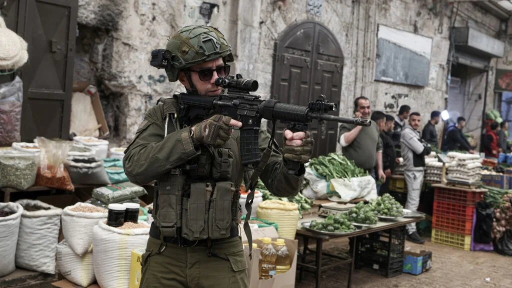 An armed Israeli soldier raises his rifle as he and his comrades patrol through the market in the Old City of Nablus, in the northern Israeli-occupied Palestinian West Bank on April 12, 2026.