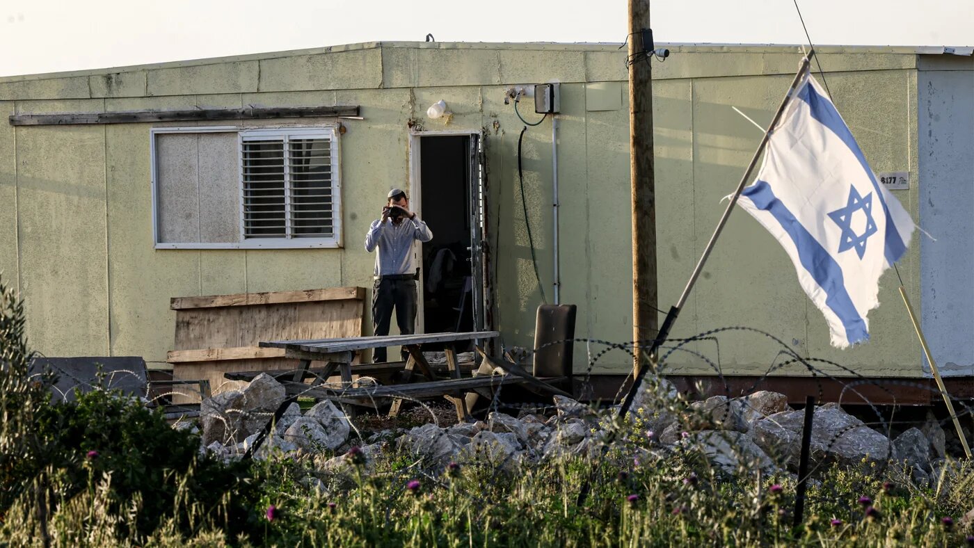An Israeli settler at the Karmel outpost records activity in the Palestinian village of Um el-Kheir, south of Yatta in the occupied West Bank, 14 April 2026 (Hazem Bader/AFP)